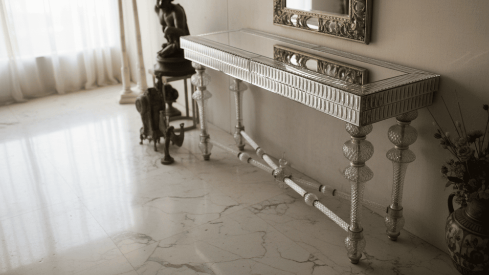 Decorative console table with intricate design in a room with marble floor and curtains.