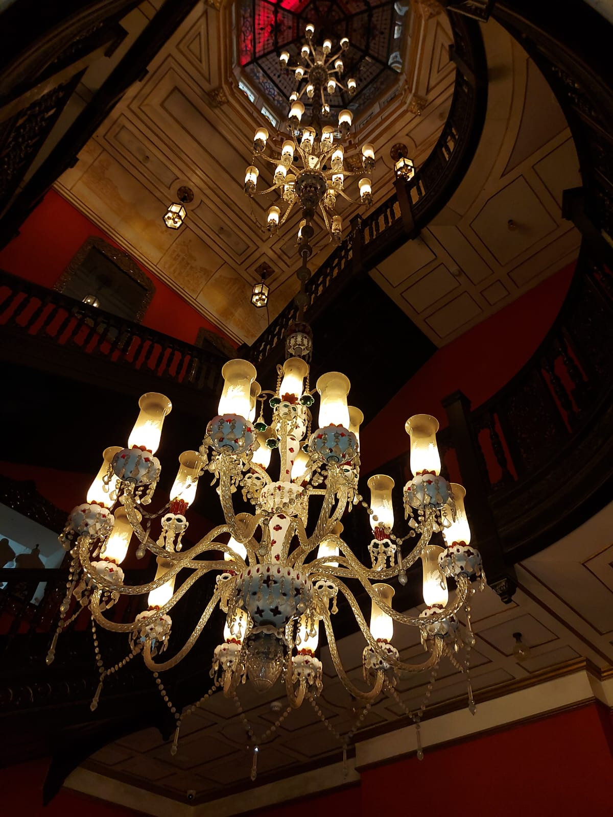 Illuminated glass chandeliers suspended within a tall stairwell.